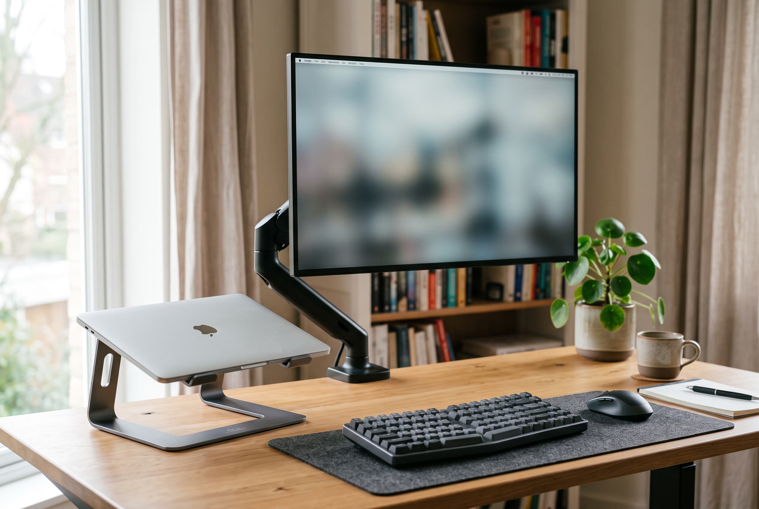 Home office desk with monitor raised to eye level beside laptop stand and external keyboard