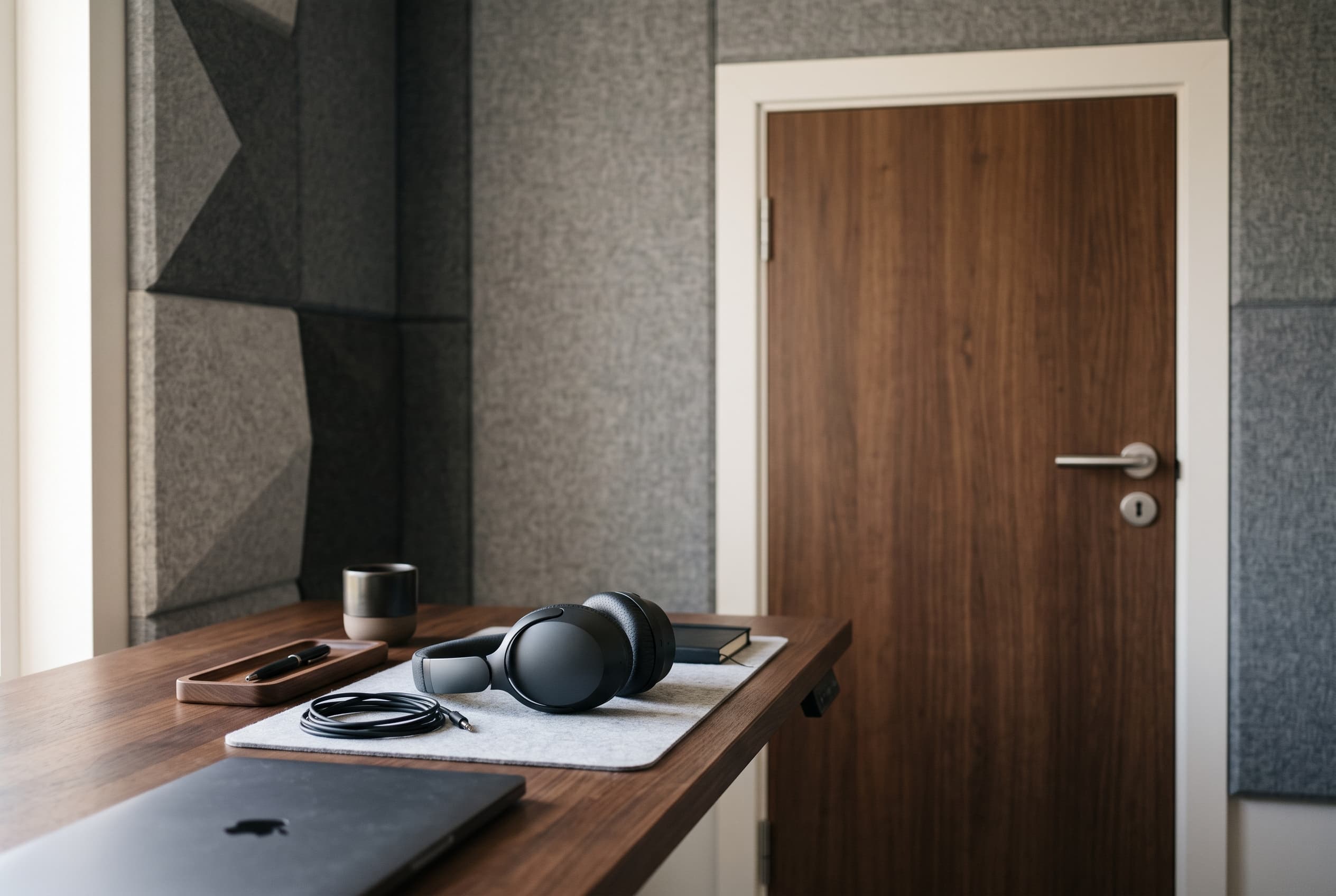 Desk with ANC headphones beside acoustic wall panels and a sealed office door